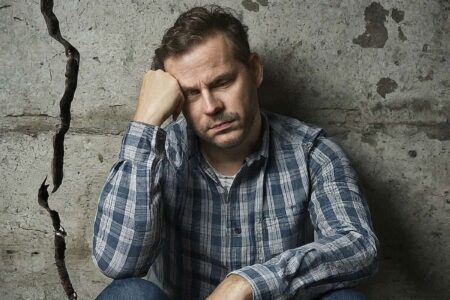 Image of a man sitting next to a large wall crack, looking regretful.