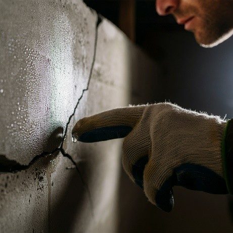 Close-up of a hand pointing to a moisture-laden crack in a basement foundation wall